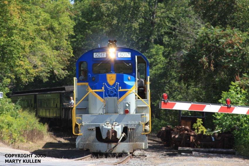 Photo of D & U RS36 #5017 and its train cross the Rte. 28 grade crossing